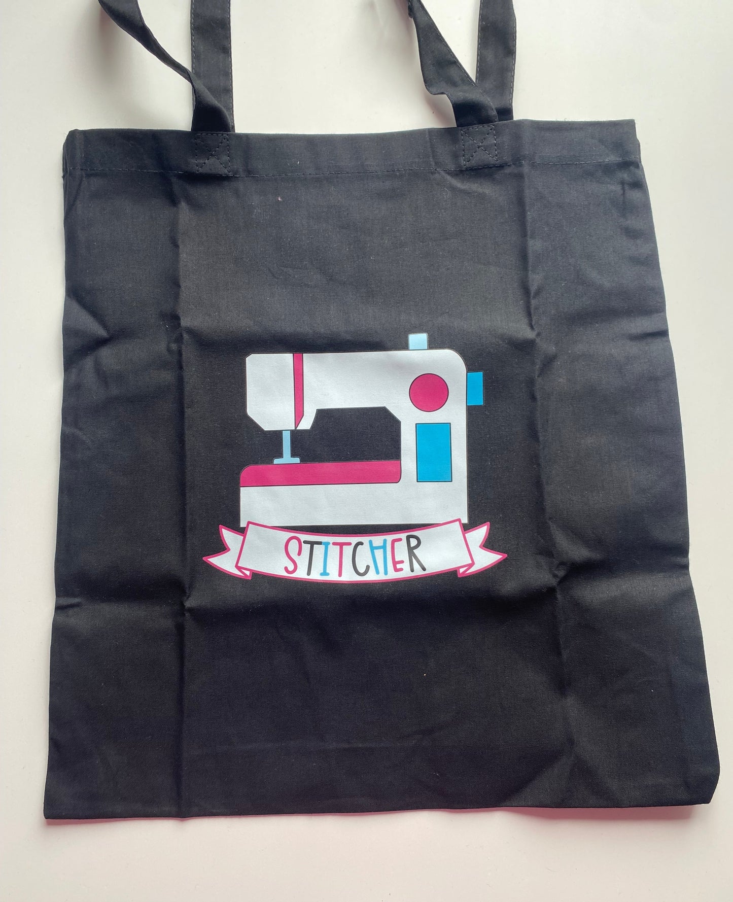 Black tote bag with a sewing machine design and 'Stitcher' text on a white background