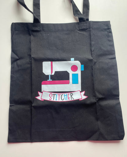 Black tote bag with a sewing machine design and 'Stitcher' text on a white background